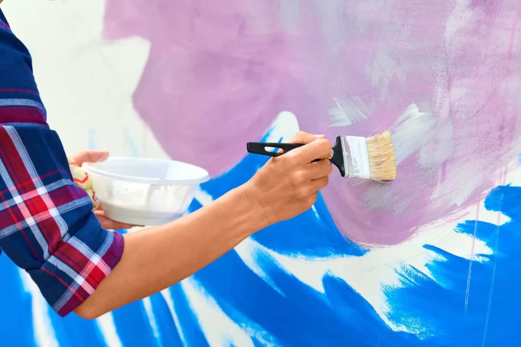 female-artist-working-on-abstract-acrylic-painting-hand-holding-paint-brush-large-canvas-outdoor